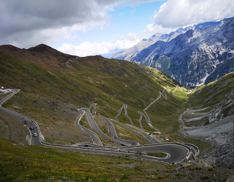 Elevated view of the Stelvio Pass hairpin switchbacks with cars climbing the mountain road