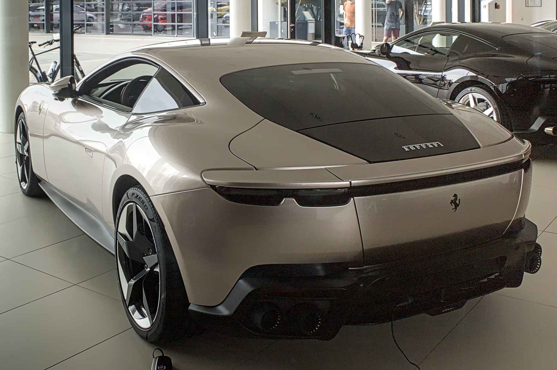 Champagne-colored Ferrari Amalfi coupe, rear three-quarter view, in a dealership showroom