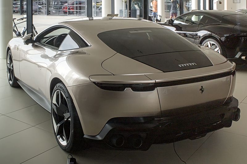 Champagne-colored Ferrari Amalfi coupe, rear three-quarter view, in a dealership showroom