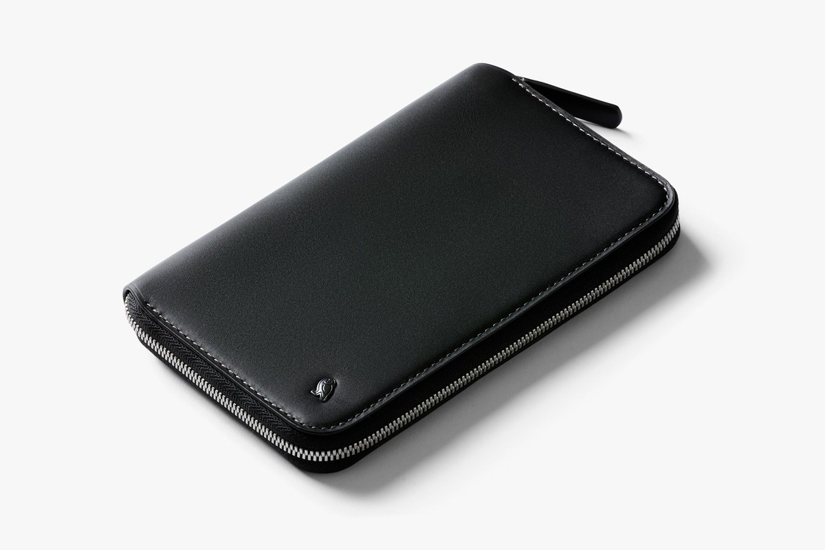 The Bellroy Travel Folio in eco-tanned leather photographed open, showing the two passport pockets, card slots, flat-bill storage and the built-in micro pen, with a passport and boarding pass tucked in place