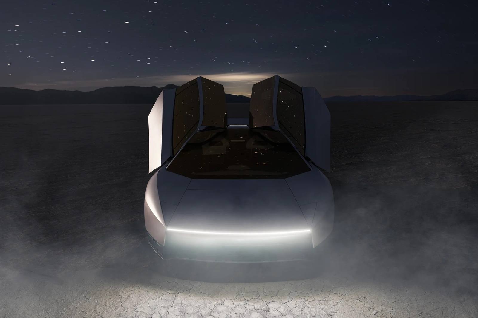 White Tesla Roadster with doors raised at night in the desert, front light bar lit
